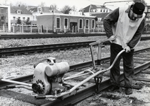 169023 Afbeelding van een wegwerker van de N.S. met een dwarsliggerboormachine tijdens werkzaamheden aan de spoorlijn ...